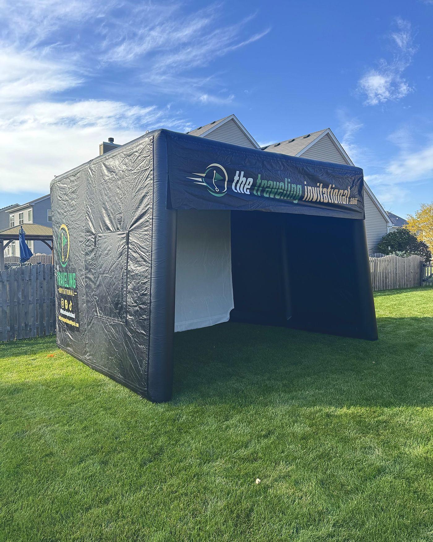 The Traveling Invitational golf bay set up on a lawn, with its open front, screen and banner